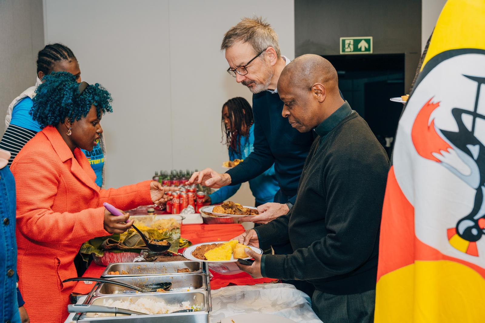 Members serving Ugandan food near a Uganda flag