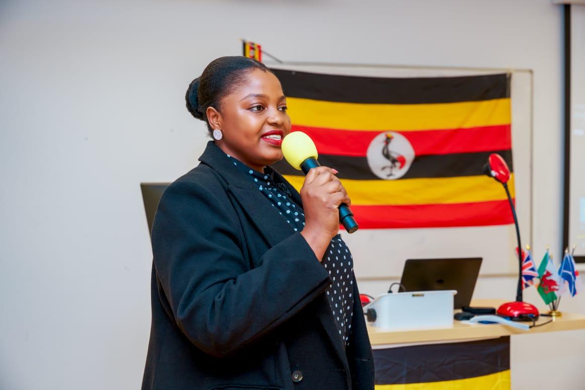 A speaker addressing guests with a microphone beside a Uganda flag