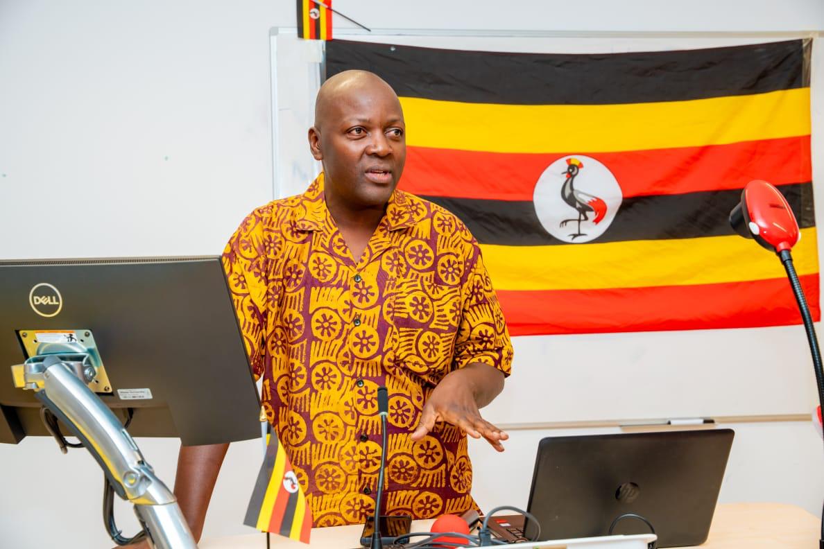 A speaker presenting in front of a Uganda flag